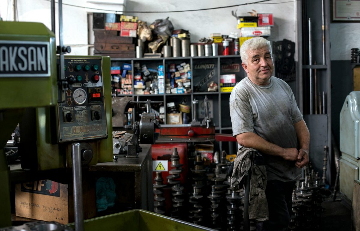 Mechanic standing in a cluttered workshop surrounded by tools and machinery, representing the hard work and dedication in automotive repair