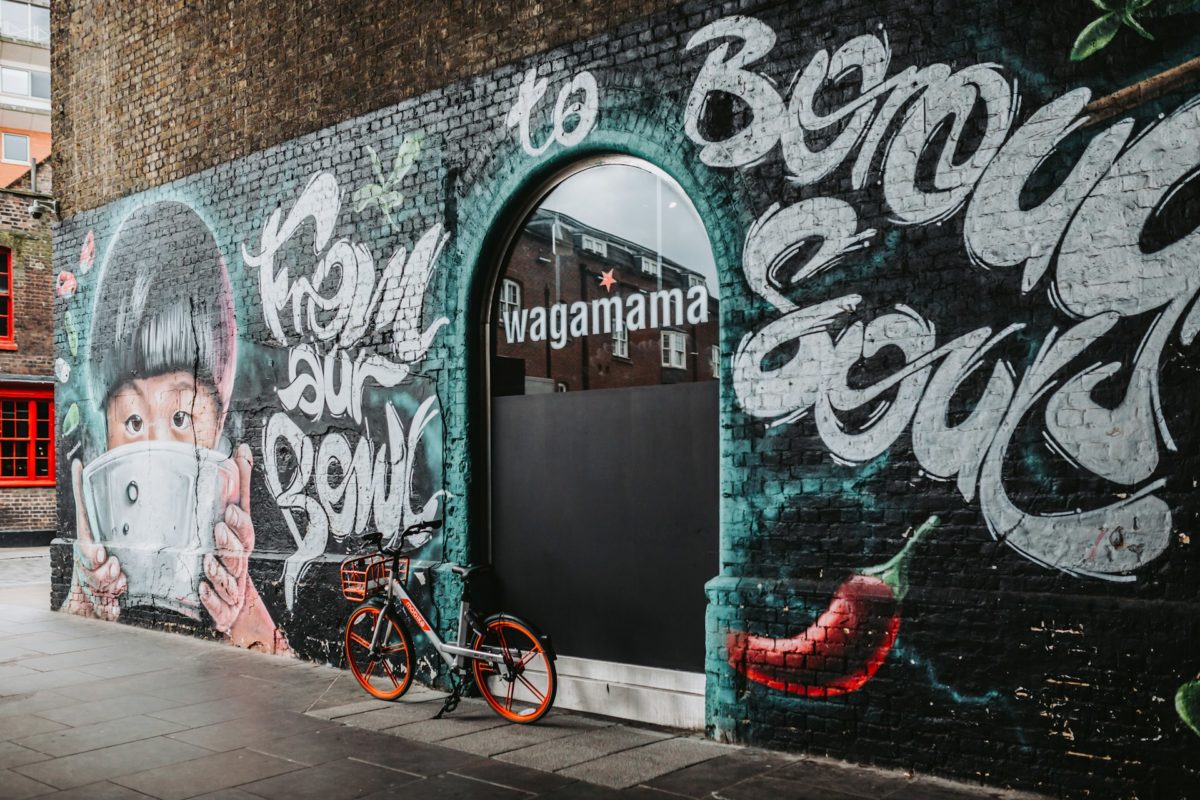 Exterior of Wagamama restaurant with colorful street art mural, including a child holding a bowl and a vibrant chili pepper, and a parked orange bicycle