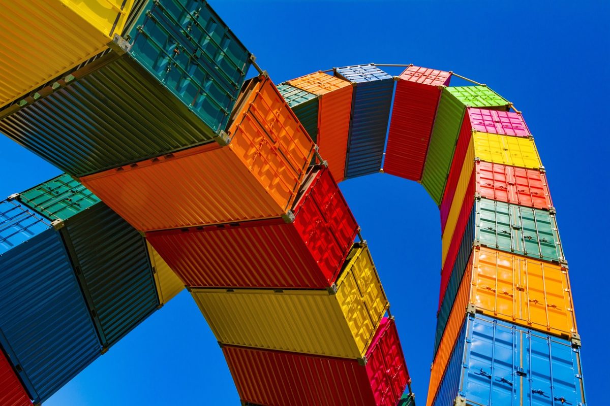 Colorful stacked shipping containers forming an arch against a clear blue sky, creating a vibrant and artistic structure