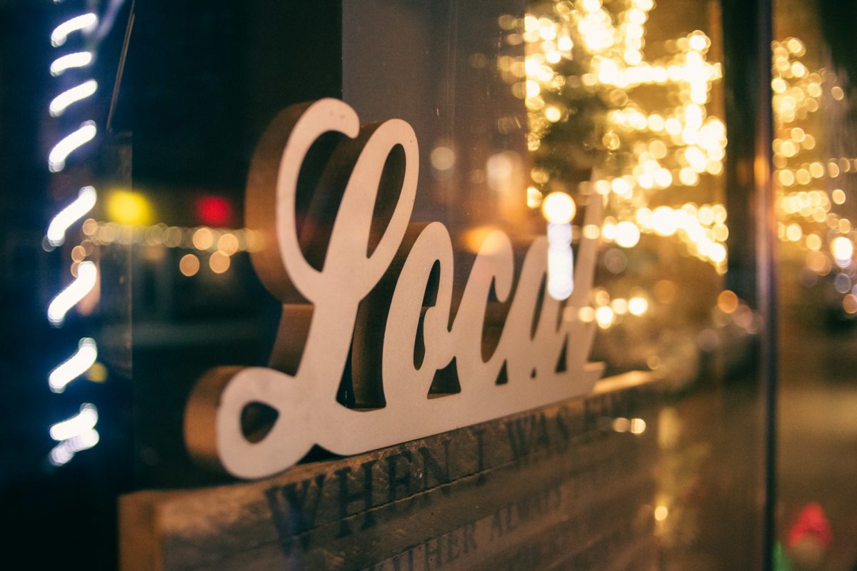 Close-up of a 'Local' sign in a warmly lit storefront window with festive bokeh lights in the background