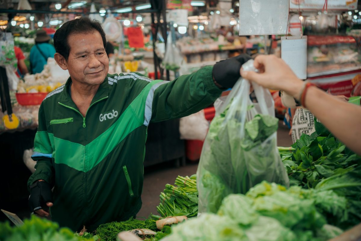 Grab delivery driver handing over a bag of fresh green vegetables at a bustling local market