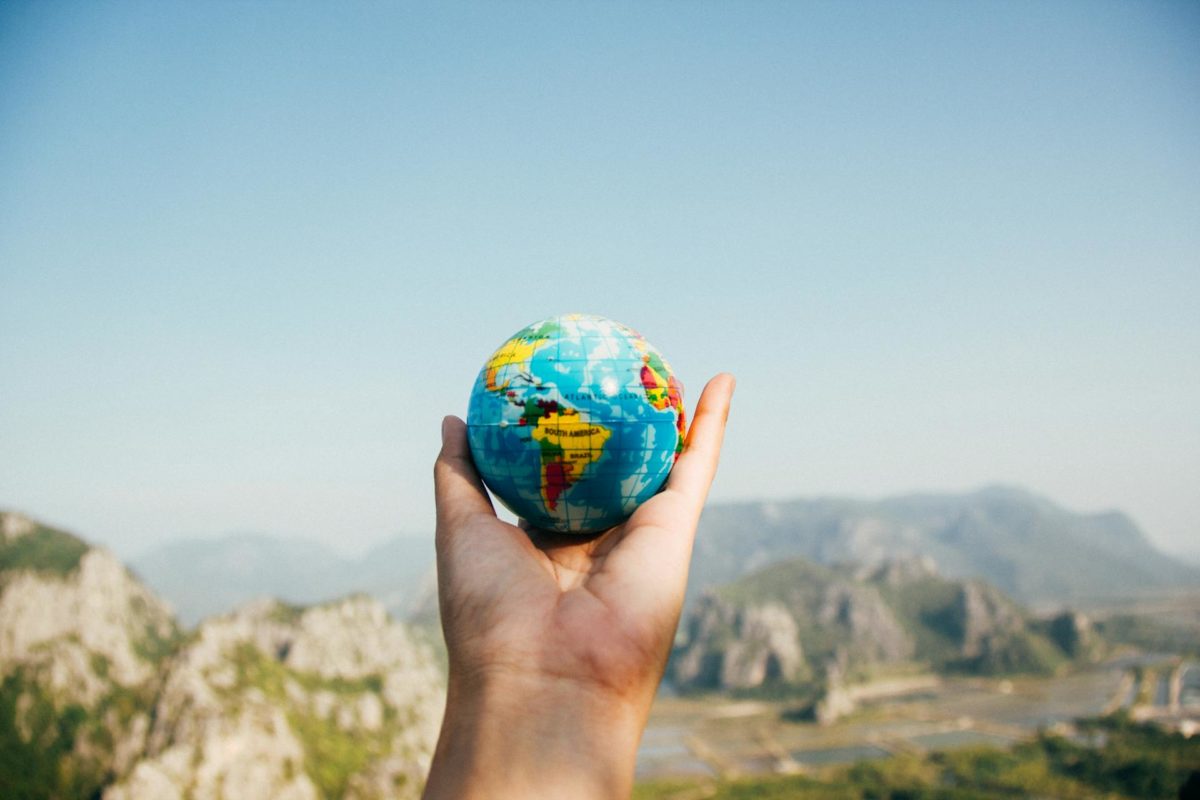 Hand holding a small globe with a scenic mountain landscape in the background, symbolizing global travel and exploration