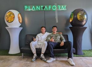 Plantaform Co-founders Alberto and Kiwa sitting on a couch with their company name in neon lights above