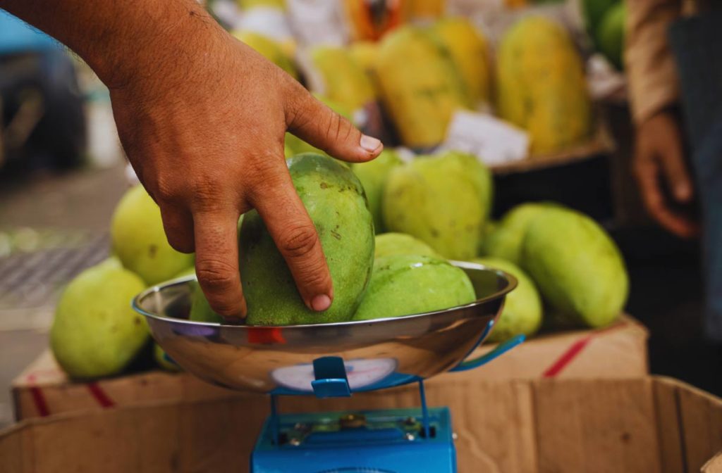 man's hand putting fruit on a scale
