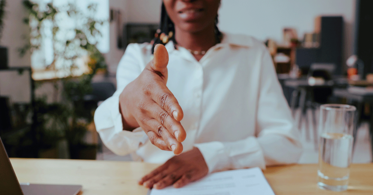 Business woman sitting across the table reaching a hand across for a handshake