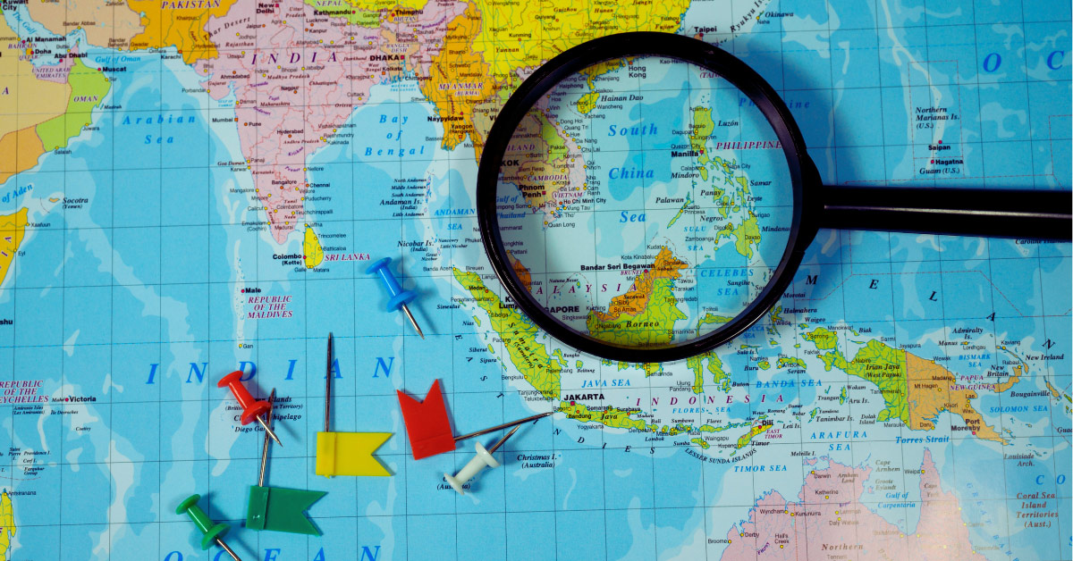 Atlas with magnifying glass, pins, focused on Southeast Asia